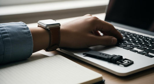 Poignet avec Apple Watch et bracelet en cuir, sur bureau; bracelet en silicone posé à côté