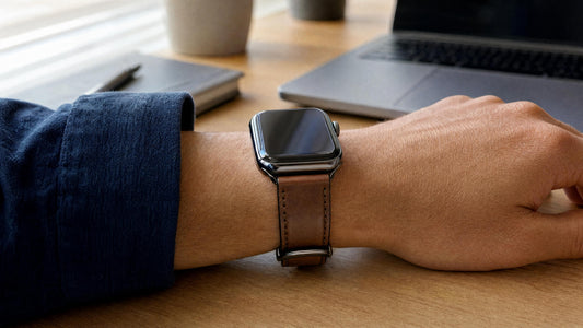 Poignet avec une Apple Watch et bracelet en cuir marron sur un bureau en bois, lumière naturelle douce