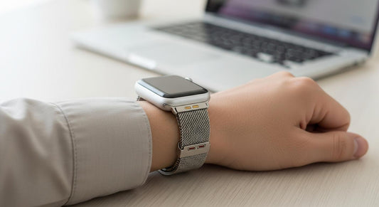 Poignet au bureau portant une Apple Watch avec bracelet milanais en acier, connecteurs visibles